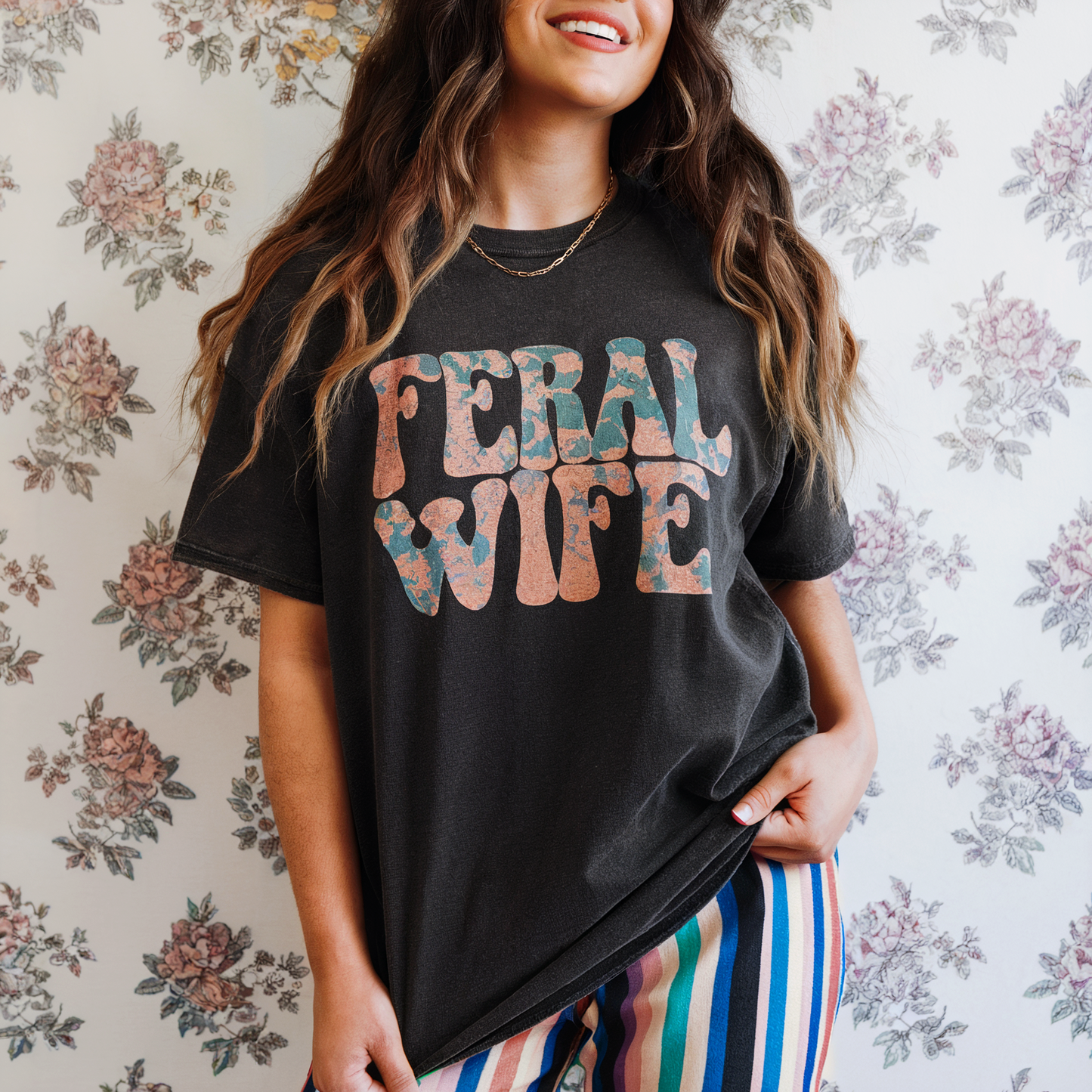 Person wearing a black t-shirt with 'FERAL WIFE' text against a floral wallpaper background