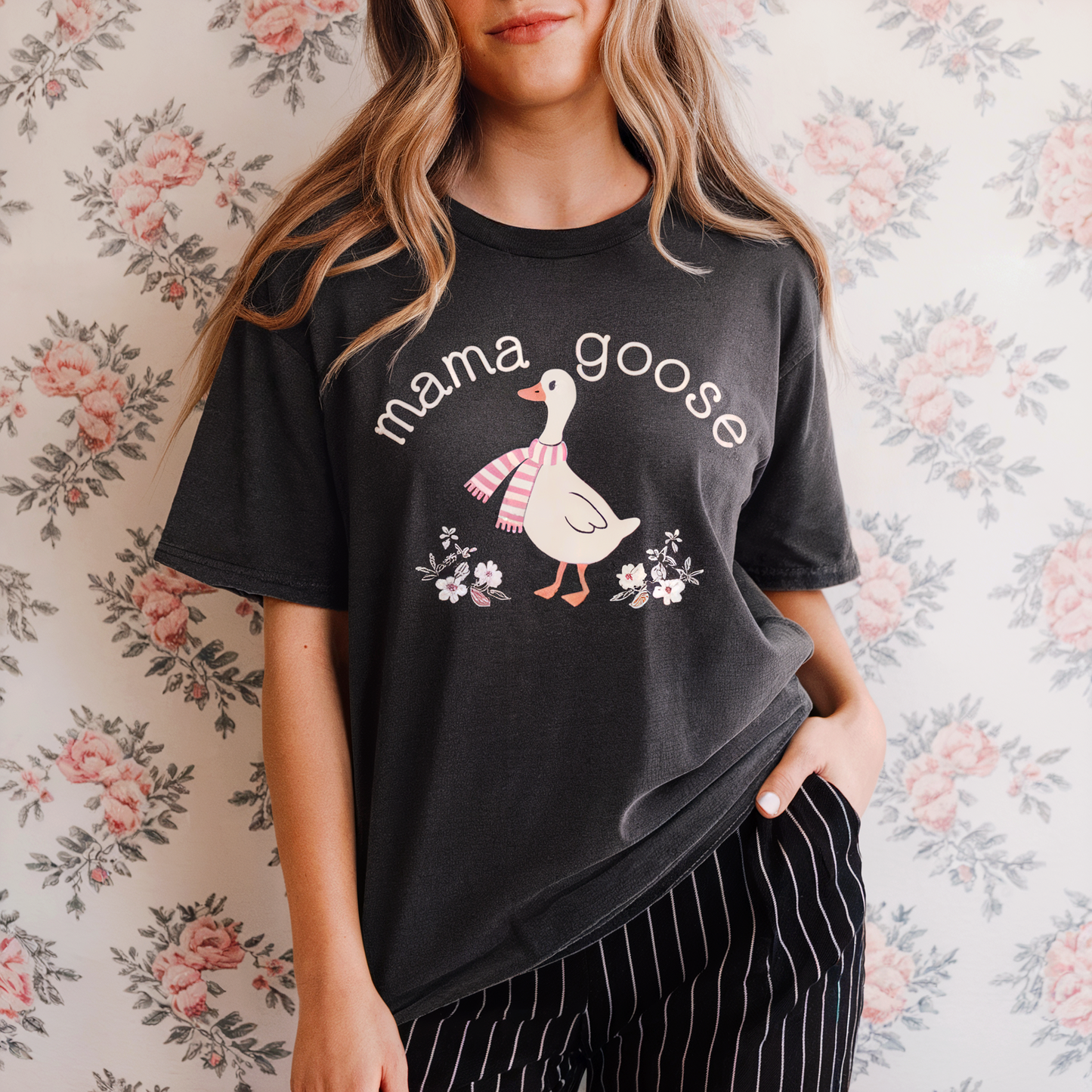 Person wearing a black t-shirt with 'mama goose' graphic against a floral background