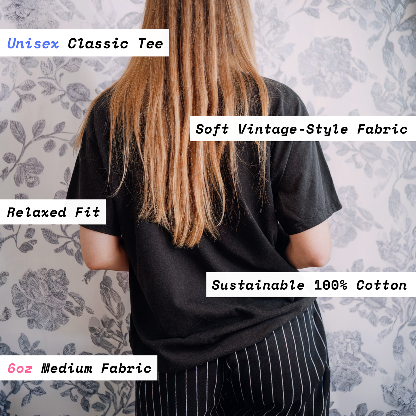 Person wearing a black unisex classic tee with text highlighting features on a floral patterned wall background.