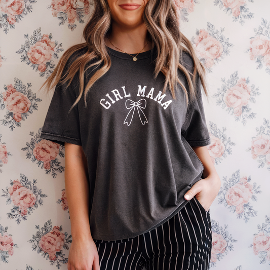Person wearing a black t-shirt with 'Girl Mama' text and a bow graphic against a floral wallpaper background.