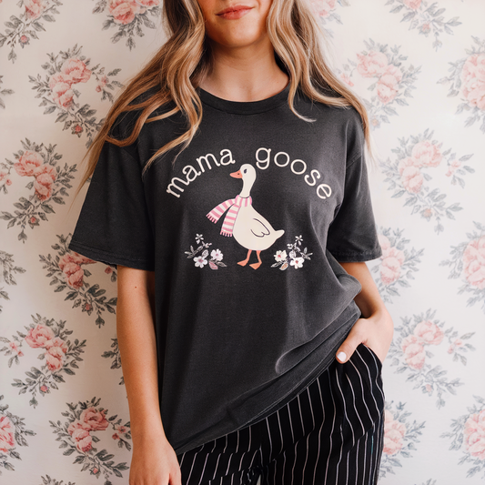 Person wearing a black t-shirt with 'mama goose' graphic against a floral background