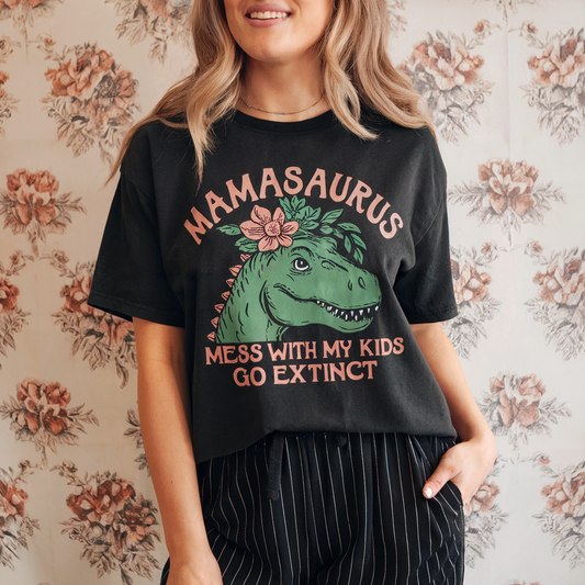 Person wearing a black t-shirt with a dinosaur graphic and text, standing against a floral wallpaper background.