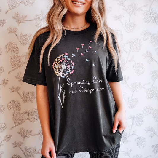 Person wearing a black t-shirt with a dandelion design and text, standing against a floral-patterned wall.